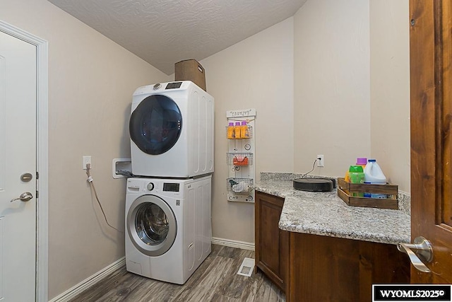 clothes washing area featuring stacked washer and dryer, a textured ceiling, baseboards, and dark wood-style flooring