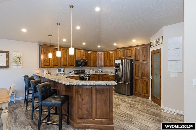 kitchen with stainless steel appliances, a peninsula, wood finished floors, and a kitchen breakfast bar