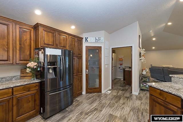 kitchen featuring stainless steel fridge, lofted ceiling, open floor plan, wood finished floors, and light stone countertops