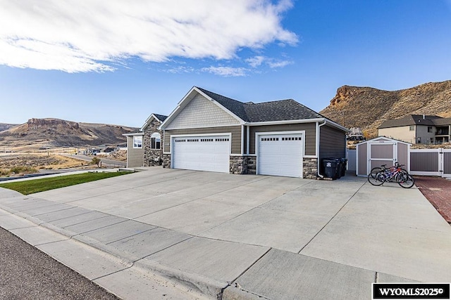 view of front of house featuring an attached garage, a storage shed, fence, a mountain view, and stone siding