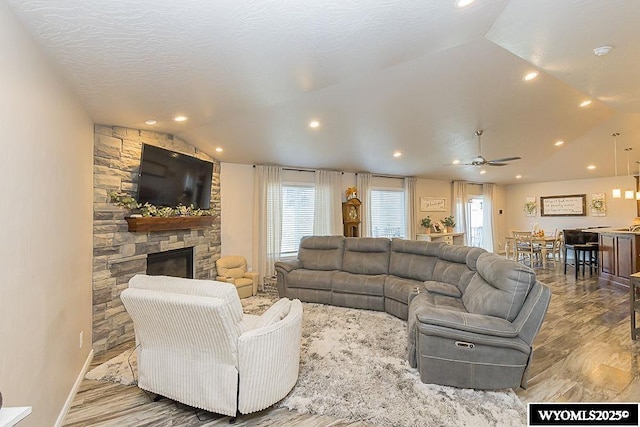 living room with a healthy amount of sunlight, vaulted ceiling, wood finished floors, and a stone fireplace