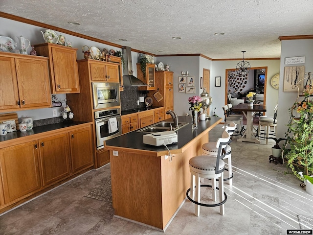 kitchen featuring brown cabinets, dark countertops, appliances with stainless steel finishes, a sink, and wall chimney exhaust hood