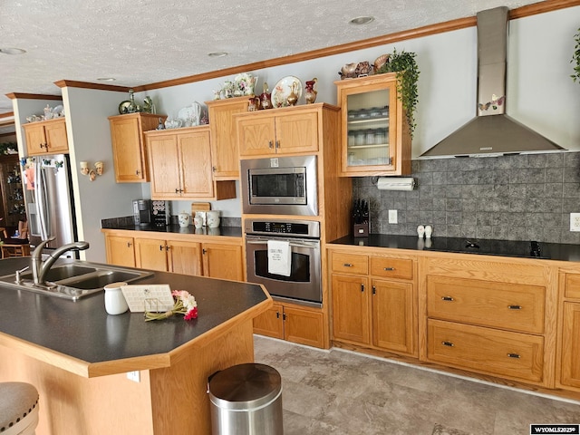 kitchen with crown molding, dark countertops, appliances with stainless steel finishes, a sink, and wall chimney range hood