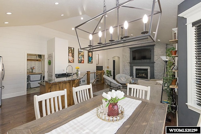 dining space with arched walkways, a large fireplace, wood walls, wood finished floors, and high vaulted ceiling