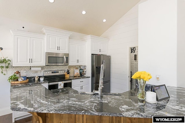 kitchen featuring tasteful backsplash, lofted ceiling, dark stone countertops, stainless steel appliances, and white cabinetry