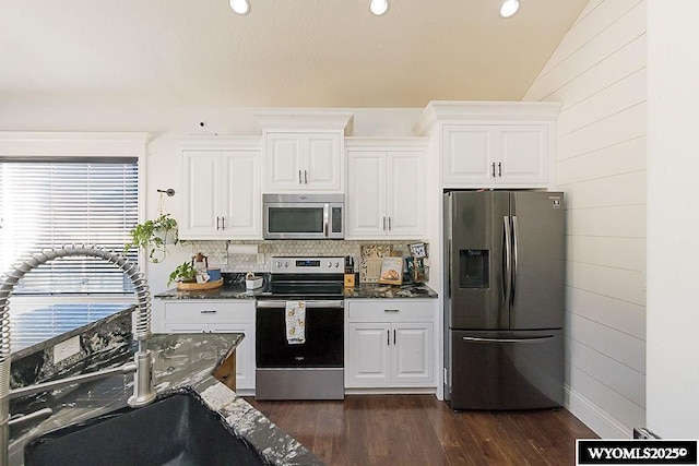 kitchen with dark wood-style floors, stainless steel appliances, white cabinetry, a sink, and dark stone counters