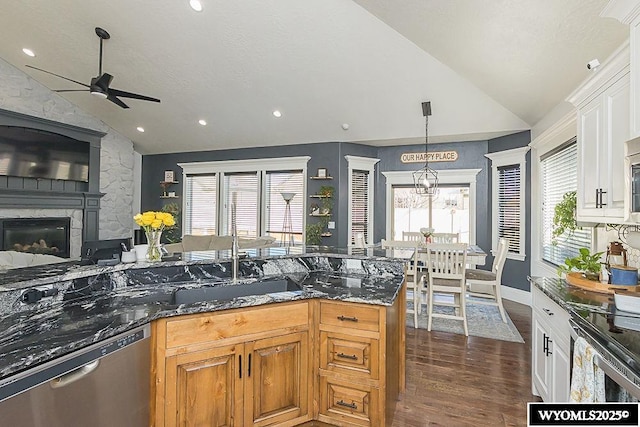 kitchen featuring lofted ceiling, stainless steel appliances, a fireplace, a sink, and dark stone counters