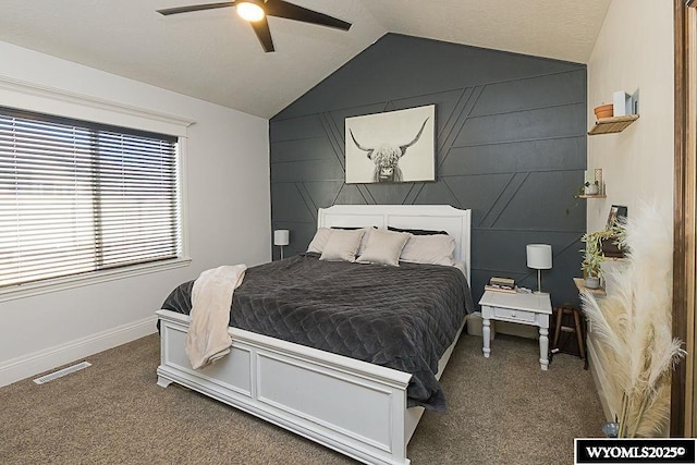 carpeted bedroom featuring ceiling fan, an accent wall, visible vents, baseboards, and vaulted ceiling