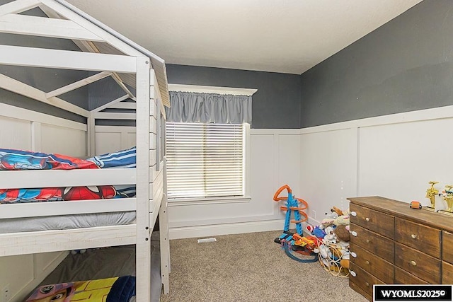 bedroom with a wainscoted wall, a decorative wall, and carpet flooring