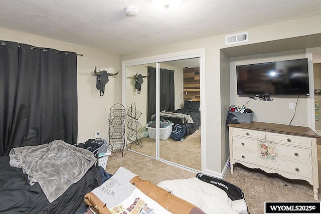 carpeted bedroom featuring a textured ceiling, a closet, visible vents, and baseboards