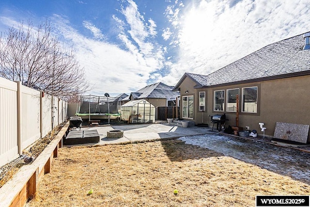 view of yard featuring a trampoline, a fenced backyard, a patio, and an outdoor structure