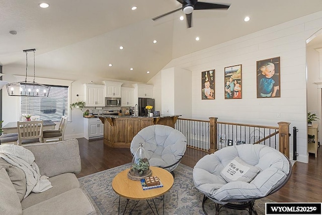 living room featuring recessed lighting, high vaulted ceiling, dark wood-type flooring, and ceiling fan with notable chandelier