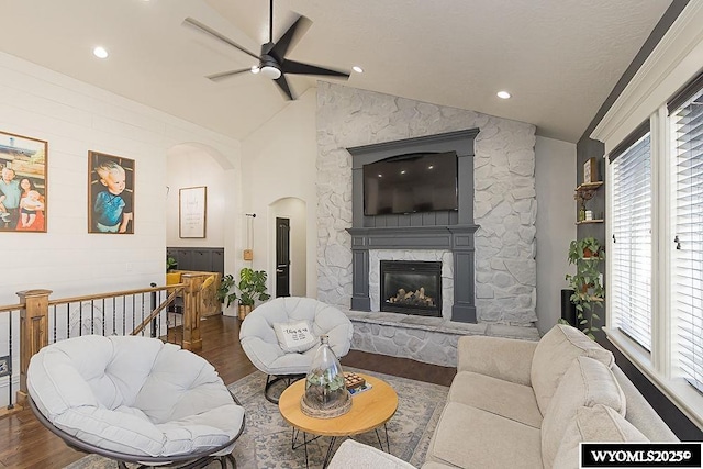 living room with ceiling fan, arched walkways, a fireplace, wood finished floors, and vaulted ceiling