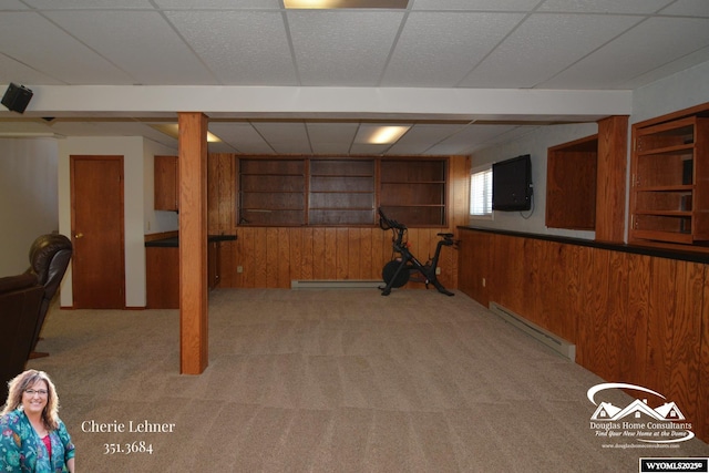 below grade area featuring a paneled ceiling, wood walls, a baseboard radiator, and light colored carpet