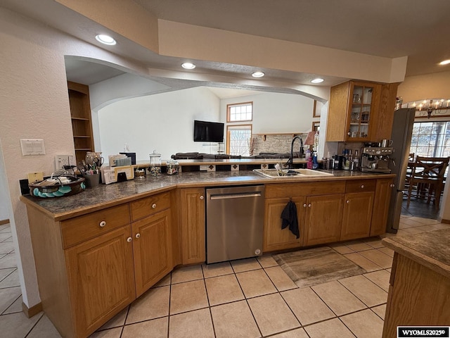 kitchen featuring a sink, a healthy amount of sunlight, stainless steel dishwasher, dark countertops, and glass insert cabinets