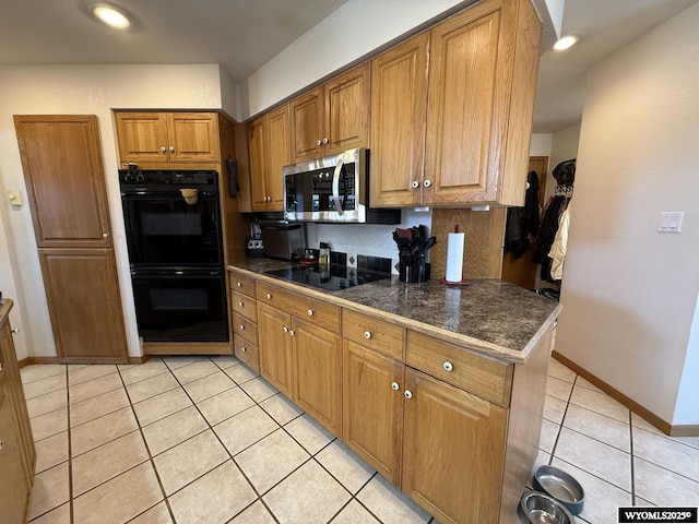 kitchen with light tile patterned floors, baseboards, dark countertops, brown cabinets, and black appliances