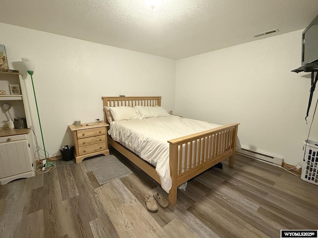 bedroom featuring a textured ceiling, a baseboard radiator, wood finished floors, and visible vents