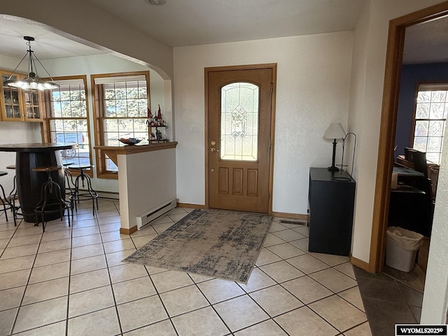 entrance foyer with a baseboard heating unit, light tile patterned floors, arched walkways, and baseboards