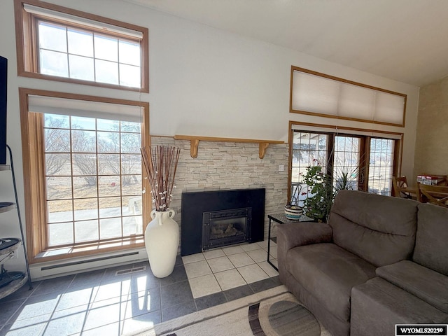 tiled living area with a baseboard heating unit, a stone fireplace, visible vents, and a healthy amount of sunlight