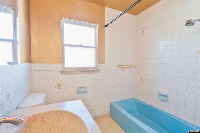 full bathroom featuring a wainscoted wall, tile walls, shower / bathing tub combination, toilet, and a sink