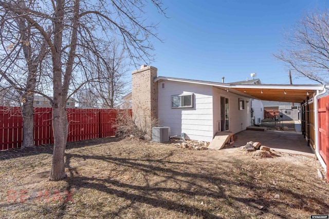 rear view of property with a carport, cooling unit, a fenced backyard, and a chimney