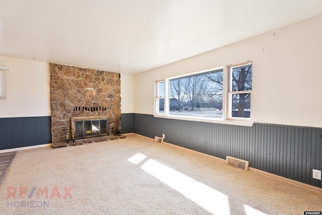 carpeted living area with a wainscoted wall, a stone fireplace, and visible vents