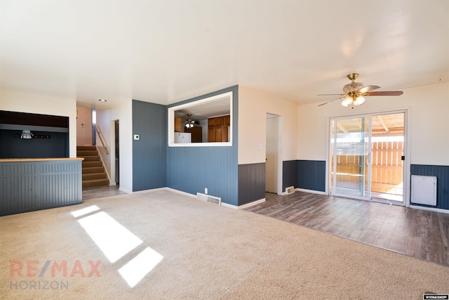 unfurnished living room with visible vents, a ceiling fan, a wainscoted wall, carpet, and stairs