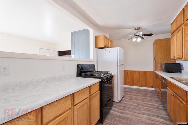 kitchen featuring light wood finished floors, wainscoting, ceiling fan, light countertops, and black appliances