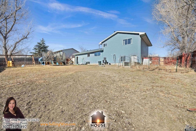 rear view of property featuring a trampoline, a playground, and fence