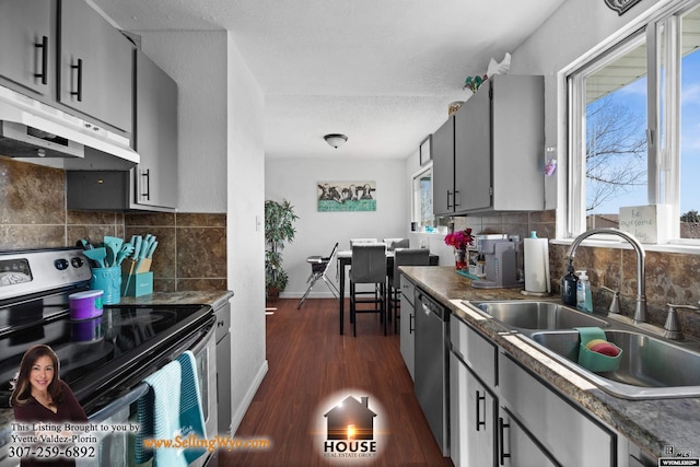 kitchen with dark countertops, under cabinet range hood, stainless steel appliances, and a sink