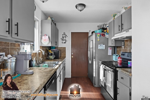 kitchen featuring appliances with stainless steel finishes, dark wood-type flooring, gray cabinets, under cabinet range hood, and a sink