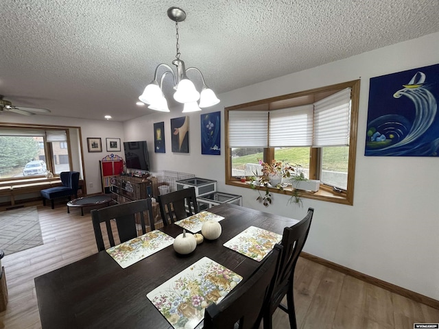 dining room featuring ceiling fan with notable chandelier, a textured ceiling, baseboards, and wood finished floors