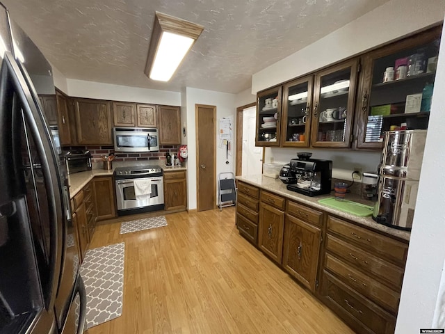 kitchen with stainless steel appliances, tasteful backsplash, light countertops, light wood-style floors, and a textured ceiling