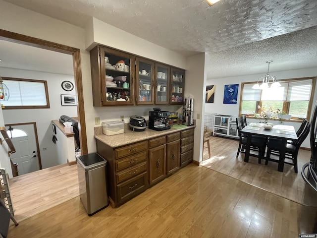 interior space featuring glass insert cabinets, light countertops, a textured ceiling, light wood-type flooring, and a notable chandelier