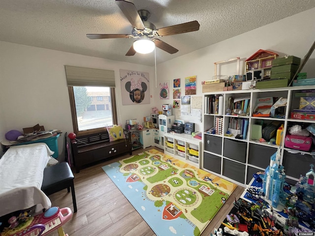 rec room with a textured ceiling, a ceiling fan, and wood finished floors