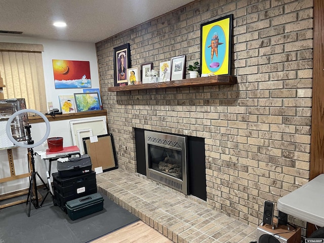 living room featuring a textured ceiling, a brick fireplace, wood finished floors, and visible vents