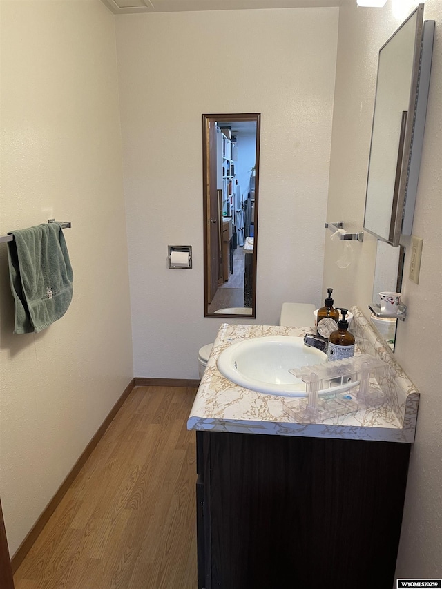 bathroom featuring toilet, baseboards, wood finished floors, and vanity