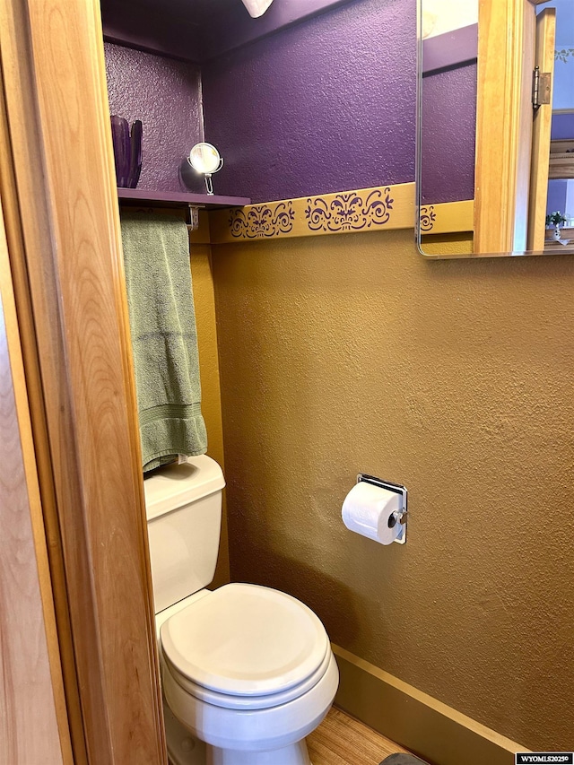 bathroom with a textured wall, toilet, and baseboards