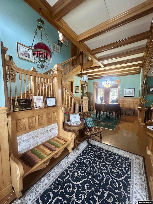 sitting room with a wainscoted wall, stairway, beam ceiling, and an inviting chandelier