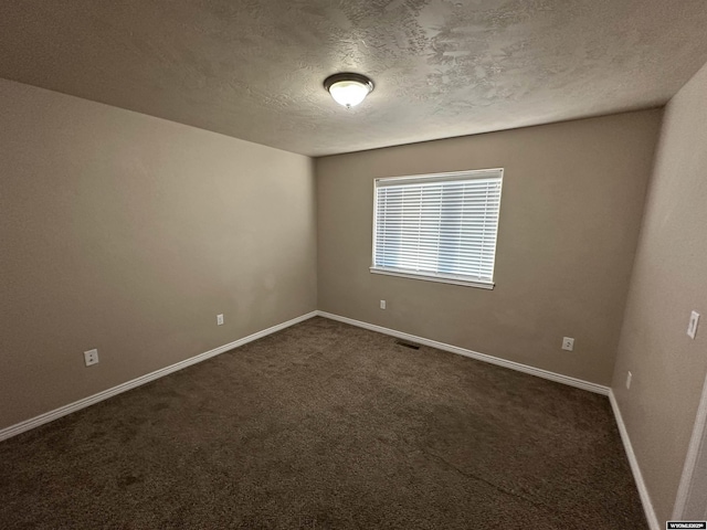 empty room featuring visible vents, dark carpet, a textured ceiling, and baseboards