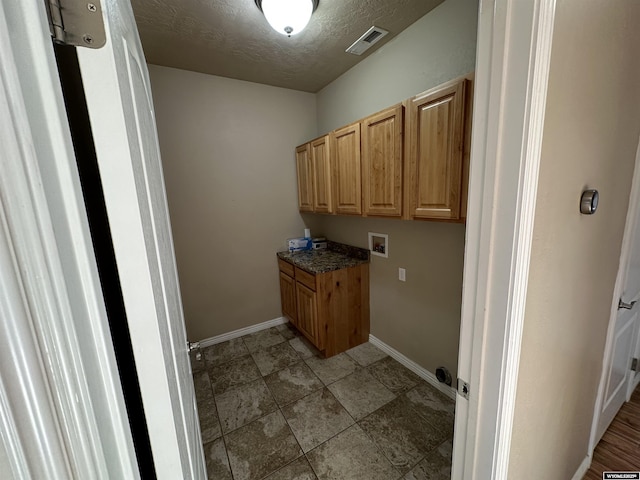 laundry area featuring a textured ceiling, washer hookup, visible vents, baseboards, and cabinet space