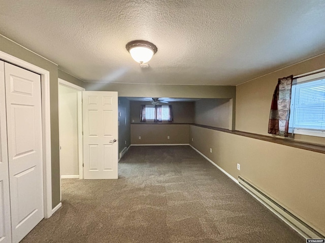 basement with a textured ceiling, dark colored carpet, a baseboard radiator, and baseboards