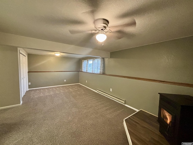 interior space with carpet, baseboard heating, a wood stove, a textured ceiling, and baseboards