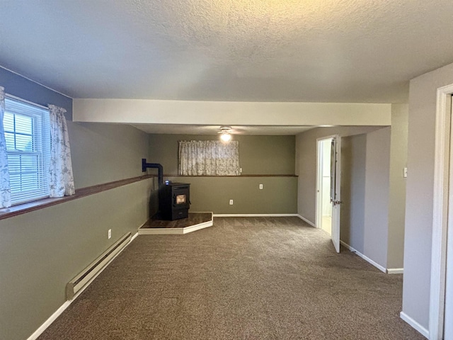 below grade area with carpet, baseboard heating, a wood stove, a textured ceiling, and baseboards