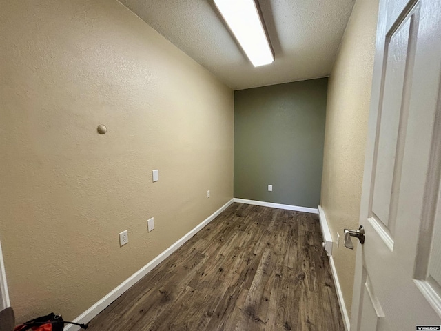 interior space featuring baseboards, dark wood finished floors, a textured ceiling, and a textured wall