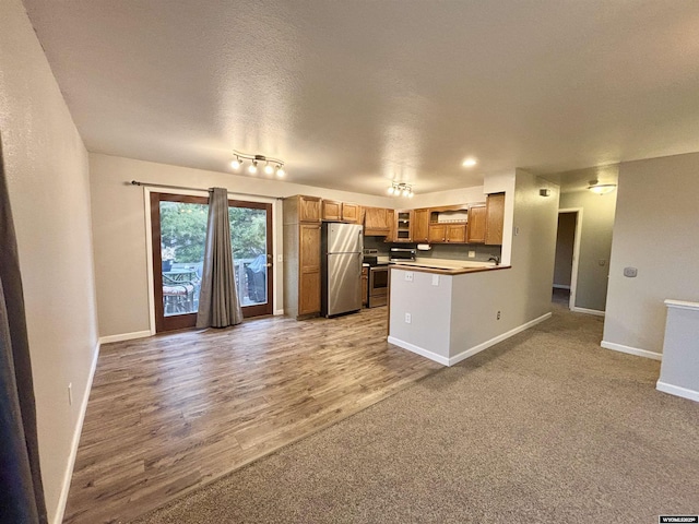 kitchen featuring stainless steel appliances, wood finished floors, baseboards, open floor plan, and brown cabinetry