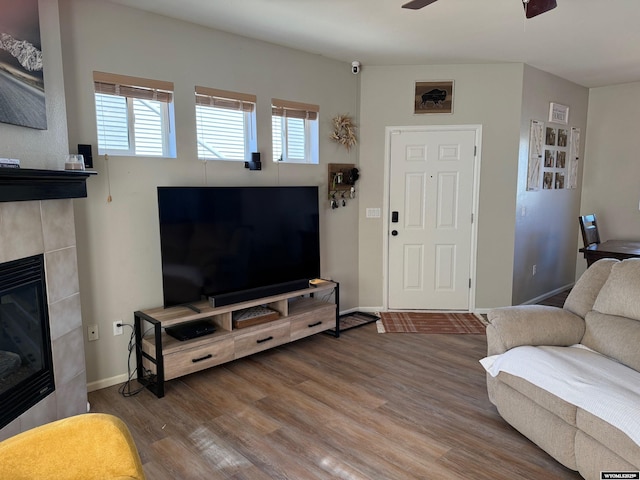 living room with baseboards, a ceiling fan, a tiled fireplace, and wood finished floors