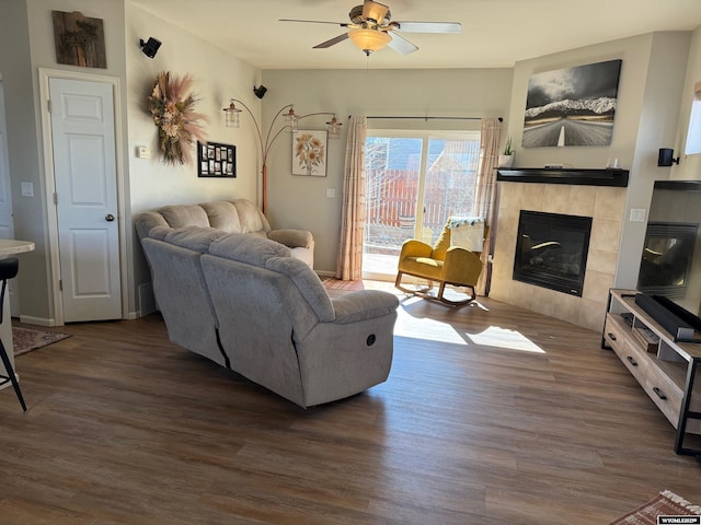 living room with dark wood-style floors, a tile fireplace, and a ceiling fan