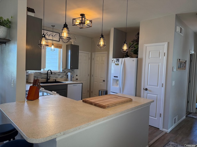 kitchen featuring a peninsula, white appliances, hanging light fixtures, and decorative backsplash