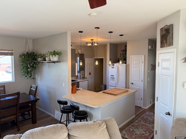 kitchen featuring a breakfast bar, dark wood-style flooring, light countertops, white appliances, and a peninsula